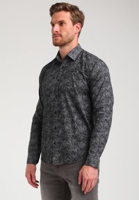 Camicia a maniche lunghe con bottoni di colore nero, caratterizzata da un motivo astratto testurizzato. Presenta un colletto classico e una tasca sul petto. Tessuto liscio.