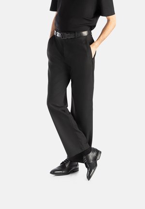 Schwarze maßgeschneiderte Hose mit geradem Bein, kombiniert mit einem schwarzen Gürtel und schwarzen Lederschuhen, die einen monochromen Look kreieren.