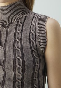 Maglione senza maniche a collo alto in taupe e beige sfumati. Presenta motivi a treccia e dettagli a coste sul colletto e sulle aperture delle braccia.