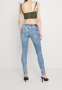 Top verde recortado con tirantes atados, combinado con vaqueros ajustados de color azul claro que tienen bolsillos y una textura desteñida. Lleva sandalias de tacón negras.