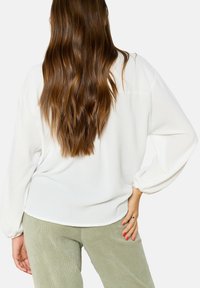 Blusa bianca, ampia e morbida, con maniche lunghe a palloncino e tessuto strutturato. Abbinata a pantaloni in corduroy verde chiaro a gamba larga.