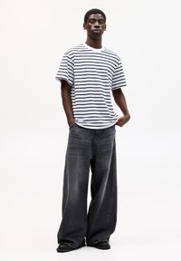 Gestreiftes, kurzärmliges T-Shirt in Weiß und Marineblau, kombiniert mit weit geschnittenen, dunkelgrauen Jeans. Das Outfit zeichnet sich durch eine lockere Passform und ein lässiges Design aus.