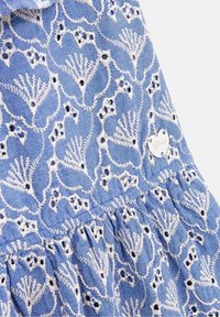 Světle modrá vyšívaná látka s květinovými vzory, s bílými nitěmi a malými černými akcenty. Obsahuje kovovou štítkovou značku.