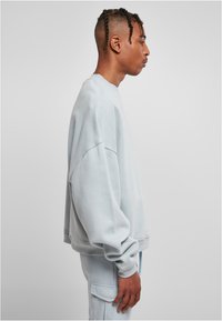 Felpa azzurra chiara con vestibilità morbida, spalle scese, polsini a costine e tessuto texturizzato, indossata con pantaloni azzurri chiari abbinati.