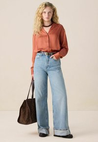 Rust-colored satin shirt, high-waisted light blue wide-leg jeans, brown leather belt, and leopard-print tote bag. Black platform shoes.