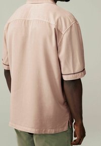 Różowa koszula z krótkim rękawem o gładkiej fakturze, z kontrastowym przeszyciem na rękawach. Luźny krój z detalem na plecach.