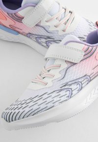 Chaussures de sport blanches avec un design texturé, mettant en avant des accents roses et violets. Comprend une sangle en Velcro, des lacets et des superpositions à motifs.