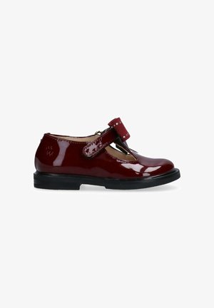 Scarpa Mary Jane in pelle verniciata bordeaux con punta rotonda, cinturino in velcro e suola in gomma nera. Caratterizzata da cuciture decorative e borchie.