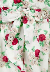 Kukkamekko kevyestä kankaasta, jossa on punaisia ja vaaleanpunaisia ruusuja vihreillä lehdillä. Sisältää solmiomaisen vyön vyötäröllä yksityiskohtana.