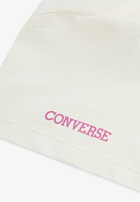Tissu en coton couleur crème avec une texture lisse, présentant le mot "CONVERSE" en lettres roses en gras près du bord inférieur.