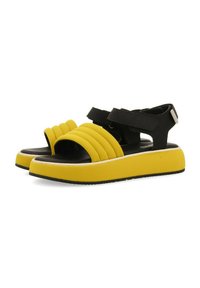 Las sandalias de plataforma negras y amarillas presentan un diseño ribeteado amarillo en la parte delantera, correas negras ajustables y una suela gruesa con detalles texturizados.