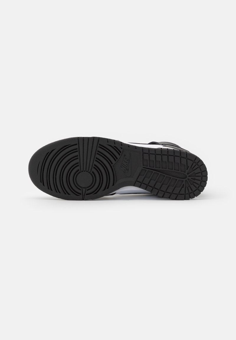 Suela de zapato de goma negra con un patrón de banda de rodadura circular y ranuras verticales, con un logotipo de Nike en relieve y acentos texturizados.