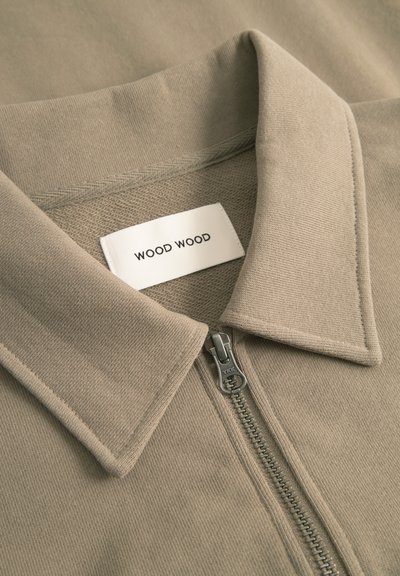 Beige színű, cipzáras ing lapos, hajtott gallérral. Ribbed textúrával, sima cipzárral rendelkezik, belsejében a "WOOD WOOD" feliratú címkével.