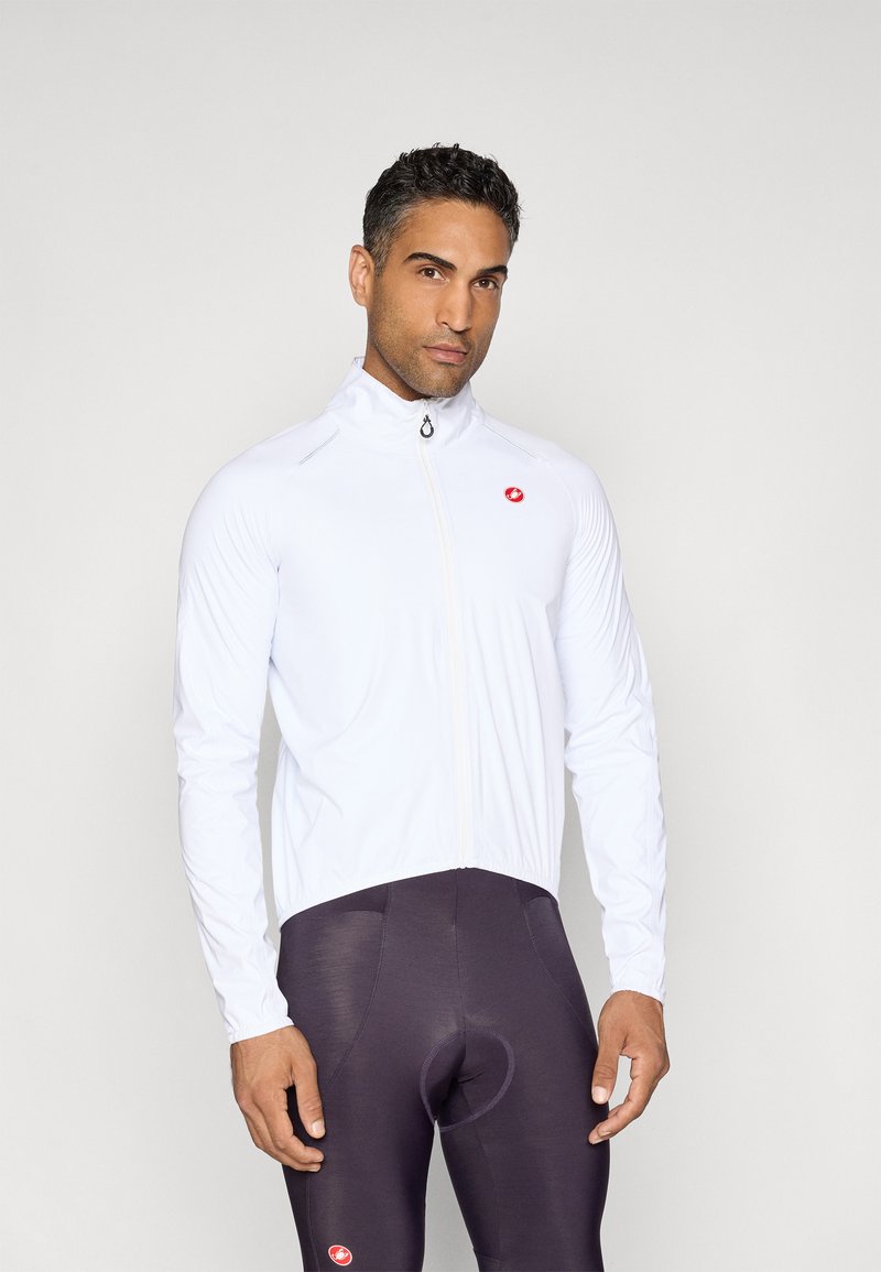 Weiße Radjacke mit hohem Kragen und durchgehendem Reißverschluss, mit rotem Logo auf der Brust. Getragen mit dunklen Sporttights. Glatte Textur.