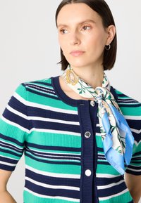 Gilet à manches courtes rayé en vert, marine et blanc avec un col rond, fermeture à boutons, et une écharpe florale nouée au cou.