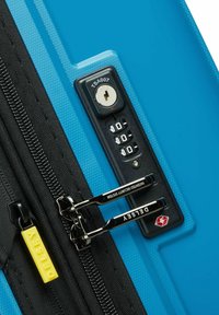 Maleta de carcasa dura en azul brillante con un acabado texturizado. Cuenta con un candado aprobado por la TSA, cremalleras negras y una pestaña amarilla con la inscripción "DELESA."