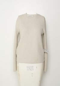 Vaaleanbeige ribattu pitkähihainen paita, jossa on pyöreä kaula-aukko. Sivuilla on merkki ja kangas on sileää. Yksinkertainen muotoilu ilman kuvioita.