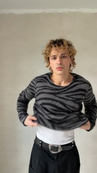 Pull rayé noir et gris en tissu doux, associé à une chemise blanche et un pantalon noir avec poches latérales et boucle de ceinture argentée.