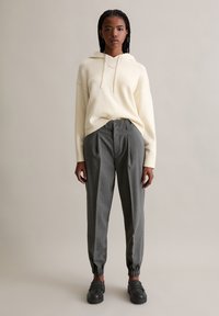 Felpa crema con cappuccio e bordi a coste; pantaloni grigi a righe sottili con fondo elastico; scarpe nere slip-on. Design semplice e moderno.