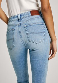 Ljusblå denimjeans med hög midja, två bakfickor och en brunt läderetikett i midjan. Slät textur med subtil blekning.
