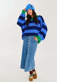 Přesně padnoucí pletený svetr s modro-zelenými pruhy, džínová sukně s knoflíkovým zapínáním, hnědé boty a modrá pletená čepice. Jemná textura, neformální styl.