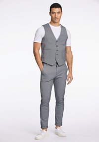 Grå väst med två framfickor, bärs över en vit t-shirt, kombinerat med matchande grå byxor och vita sneakers, med en smal passform.