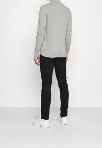 Pull gris à manches longues avec un col montant, associé à un pantalon noir slim et des baskets blanches. Texture lisse, sans motifs visibles.