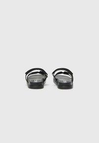 Svarta platta sandaler med en minimalistisk design, som har tunna remmar och en texturerad sula, monterade på en platt sula.