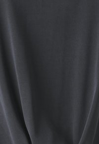 Tessuto grigio scuro con una texture liscia, che si drappeggia dolcemente con leggere pieghe. Il materiale sembra leggero e traspirante.