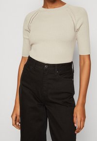 Ribbed beige sweater with a round neckline and short sleeves, paired with high-waisted black denim pants featuring standard pockets.