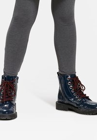 Modre lakirane gležnjarje z rdečimi vezalkami, srebrnimi očesi in debelim črnim gumijastim podplatom. Teksturna površina in podrobnost stranskega zadrge.