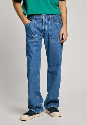 Blauwe denim jeans met een recht gesneden ontwerp. Bevat voorzakken, riemlussen en een knoopsluiting. Gemaakt in combinatie met zwarte sneakers.