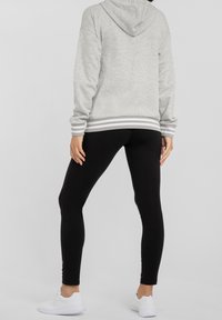 Grijze hoodie met een capuchon en gestreepte manchetten, gecombineerd met zwarte leggings. Gestyled met witte sportschoenen, wat een strakke silhouet laat zien.