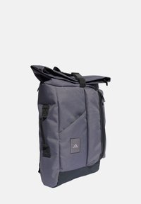 Šedý batoh s rolovacím designem, vyrobený z texturované tkaniny, s přední kapsou na zip, černými akcenty a logem na přední straně.