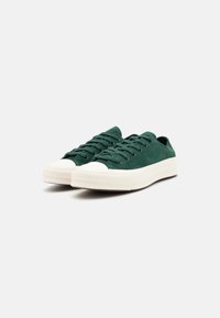 Zelené semišové tenisky s bílými gumovými špičkami a podešvemi, které mají kulaté tkaničky a texturovaný design mezipodešve.