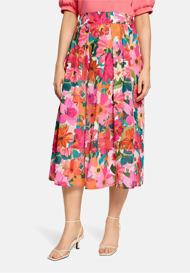 Midlang plisseret nederdel med lyserødt, orange og grønt blomsterprint, båret med nude stroppesandaler og en lyserød top med puffede ærmer.