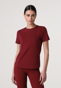 T-shirt in cotone bordeaux con scollatura a girocollo classica, maniche corte e forma aderente. Texture liscia senza motivi o accessori visibili.