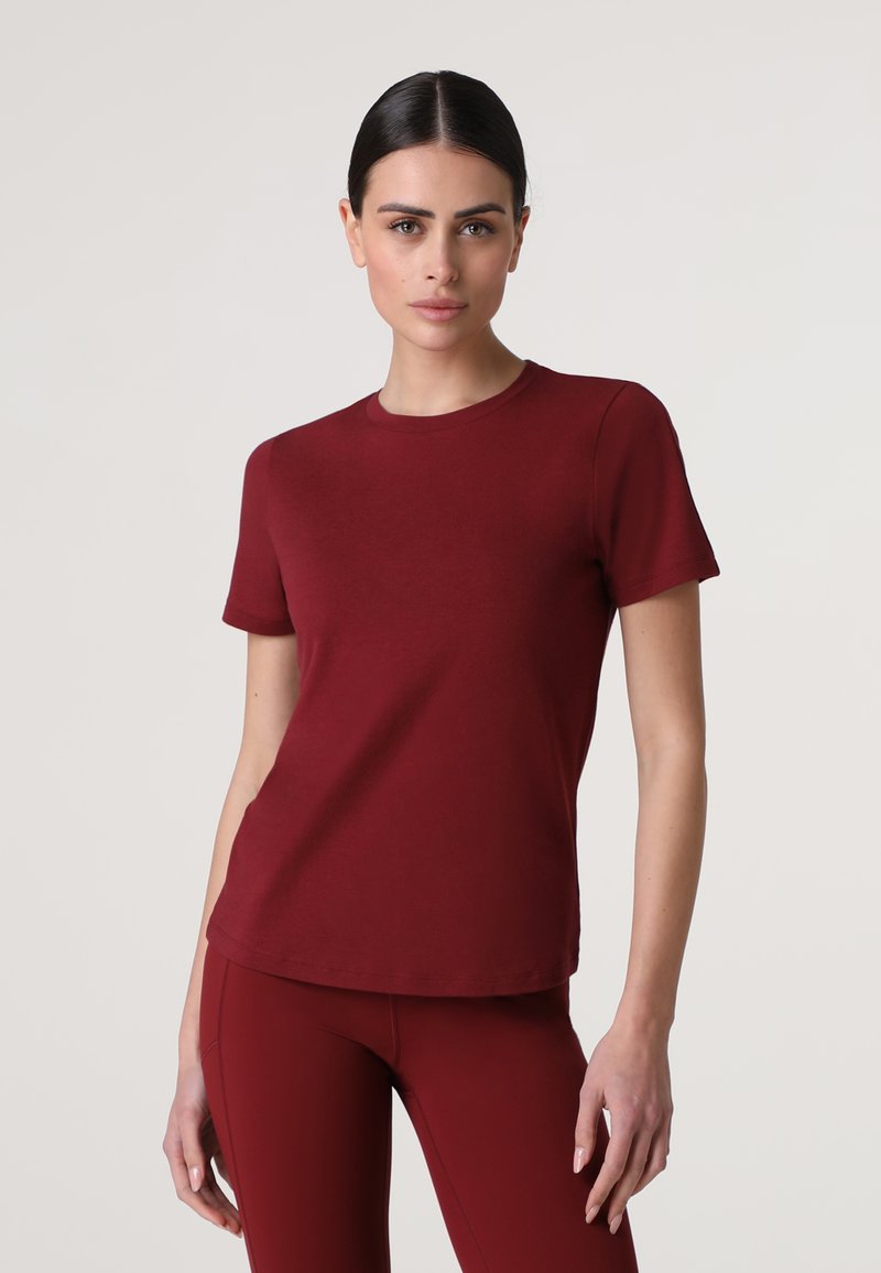 T-shirt in cotone bordeaux con scollatura a girocollo classica, maniche corte e forma aderente. Texture liscia senza motivi o accessori visibili.