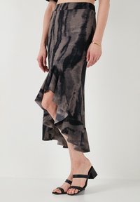 Falda ajustada de longitud media en patrón de tie-dye en negro y gris con dobladillo rizado. Tejido suave con una textura lisa. Llevada con sandalias negras de tacón bloque.