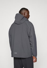 Sivi windbreaker s kapuljačom, s kontrastnim bijelim šavovima i oznakom "climaProof" blizu ruba. Opustiti kroj, lagani materijal.