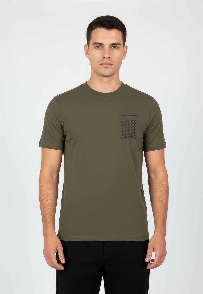 Olivově zelené tričko s krátkým rukávem z hladkého materiálu, vyznačující se kapsou na hrudi s černým kostkovaným vzorem a logem nad ní.