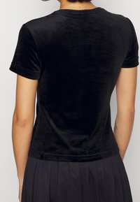 Svart sammet kortärmad T-shirt med en åtsittande design, rund halsringning, slät textur och subtil lyster, sedd bakifrån.