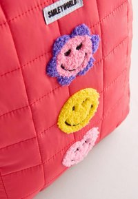 Röd quiltad väska med tre leende ansiktsmärken: rosa blomma, gul cirkel och lila blomma, alla med texturerad broderi.