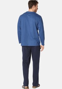 Blue long-sleeve shirt with a round neckline, paired with dark navy pants. Material appears soft and casual, complemented by tan sandals.