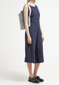 Mono culotte azul marino con escote cuadrado, combinado con una mochila gris y zapatos negros con detalle de tira. Tejido suave y corte moderno.