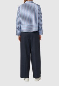 Camicia a righe blu e bianca, corta e con maniche lunghe, abbinata a pantaloni ampi blu scuro a vita alta e sneakers bianche.