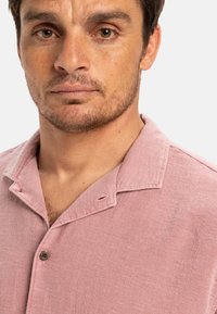 Jasnoróżowa koszulka z kołnierzykiem i zapięciem na guziki, o teksturowanej tkaninie i minimalistycznym wzorze.