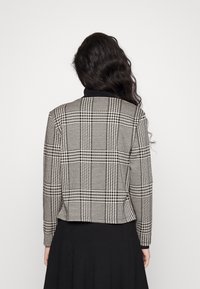 Svart och vit rutigt blazer med en strukturerad passform och kort längd, med en subtil glans och utan synlig hårdvara.