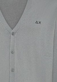 Cardigan grigio con scollo a V, chiusura con bottoni e tessuto morbido. Presenta un piccolo logo stampato a forma di triangolo con una croce sull'area del petto sinistro.