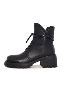 Bota de cuero negra hasta el tobillo con tacón grueso, parte delantera con cordones y detalle de cordón envolvente sobre un fondo blanco.